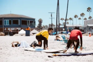 A private surf lesson instructor showing a customer how to pop up on a surfboard