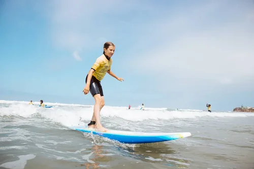 A private surf lesson customer wearing a yellow jersey and riding a wave on a foamboard.
