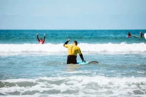 A private surf lesson customer wearing a yellow jersey cheering after getting off of a wave.