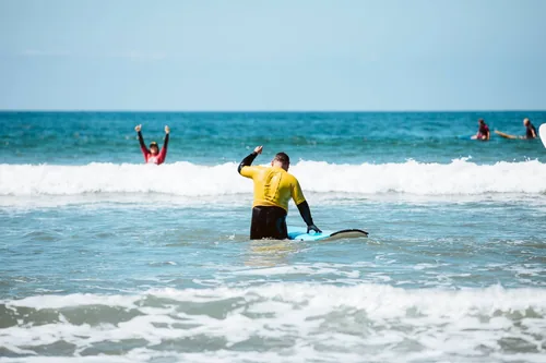 A private surf lesson customer wearing a yellow jersey cheering after getting off of a wave.