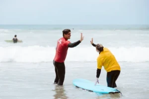 A San Diego Surf School instructor giving a high five in the shoreline to a customer during a private surf lesson in San Diego.