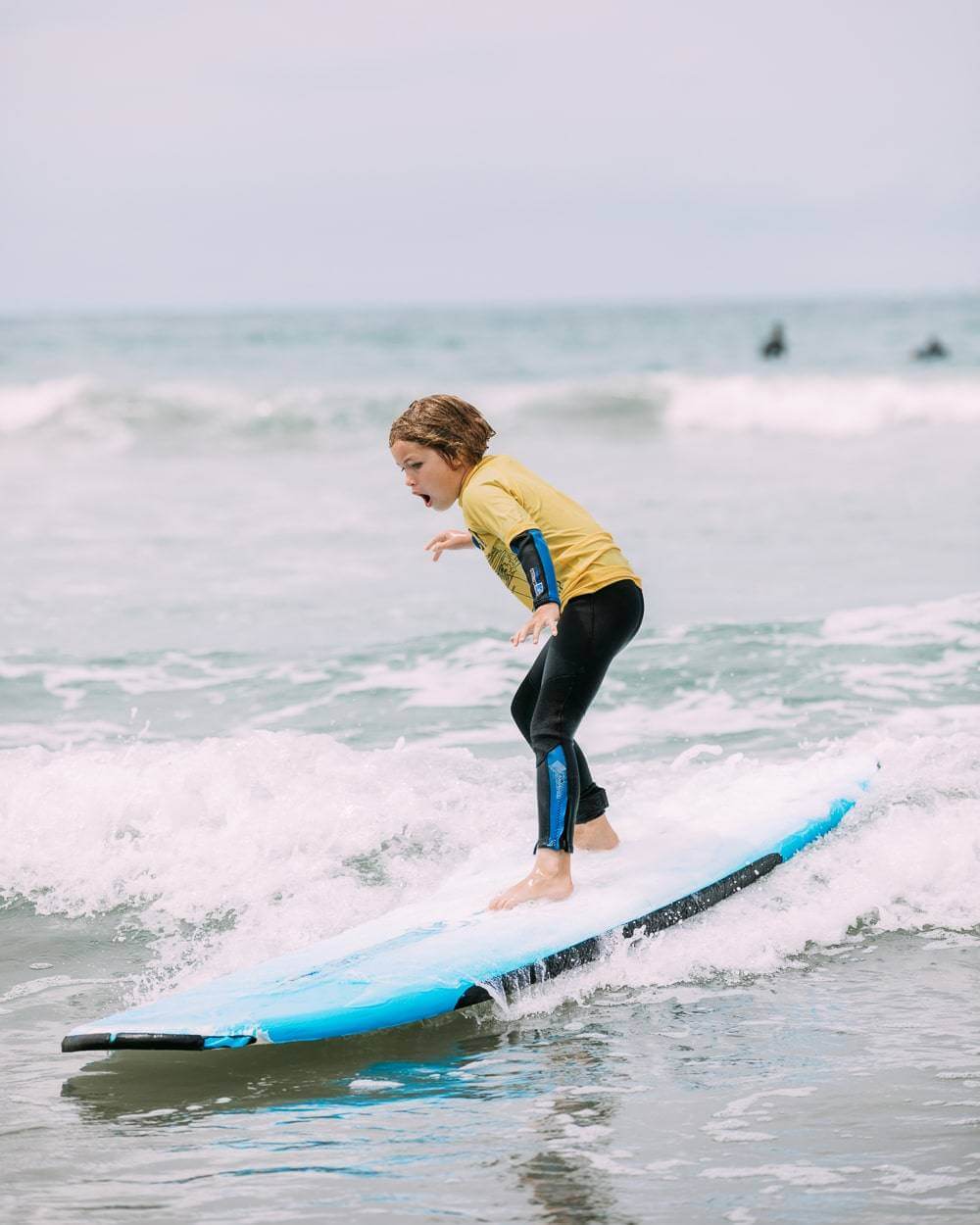 A child wearing a yellow jersey riding a wave after receiving a private surf lesson.