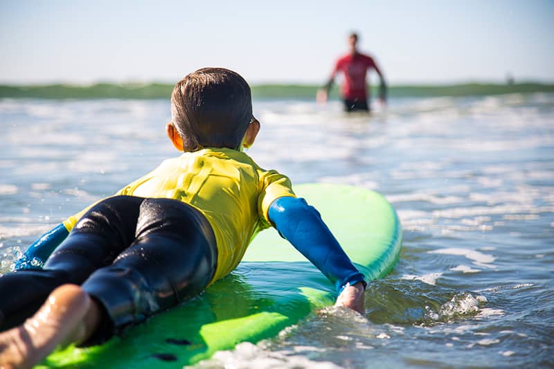 A child paddling on a surfboard in the shore towards a CPR certified instructor.