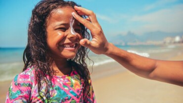 parent putting on sunscreen on smiling child's face on a beach, sunscreen for the ocean