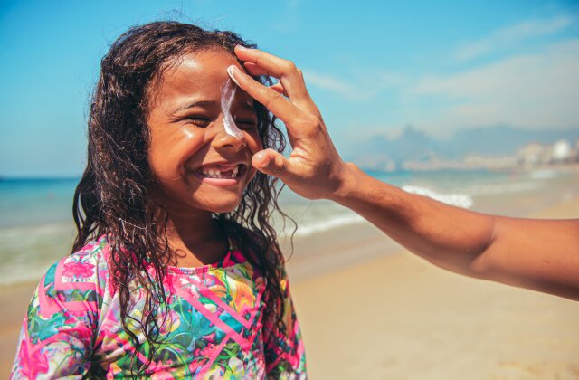 parent putting on sunscreen on smiling child's face on a beach, sunscreen for the ocean